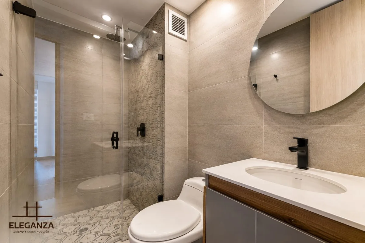 Baño con ducha en vidrio, enchape hexagonal y mesón en madera