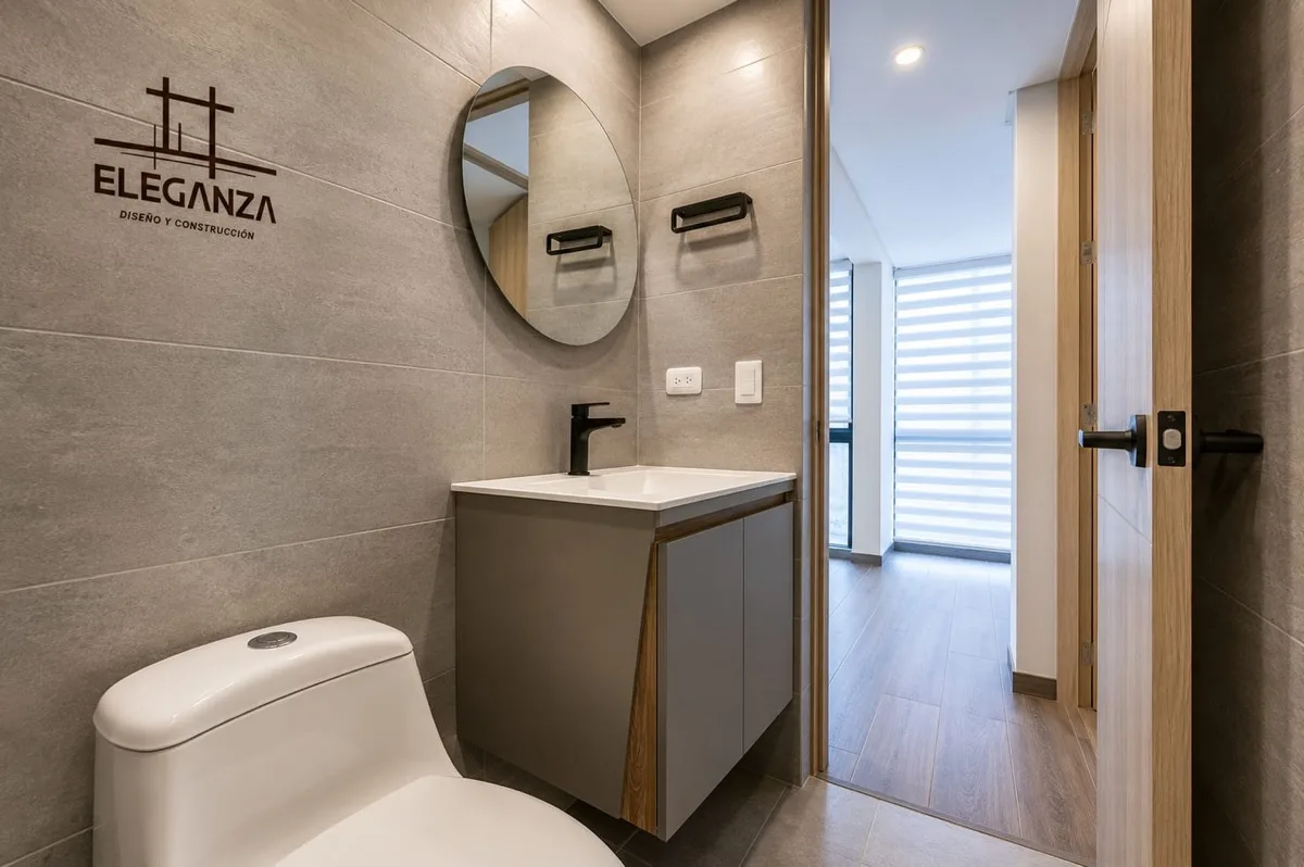 Baño social con espejo redondo y mueble gris